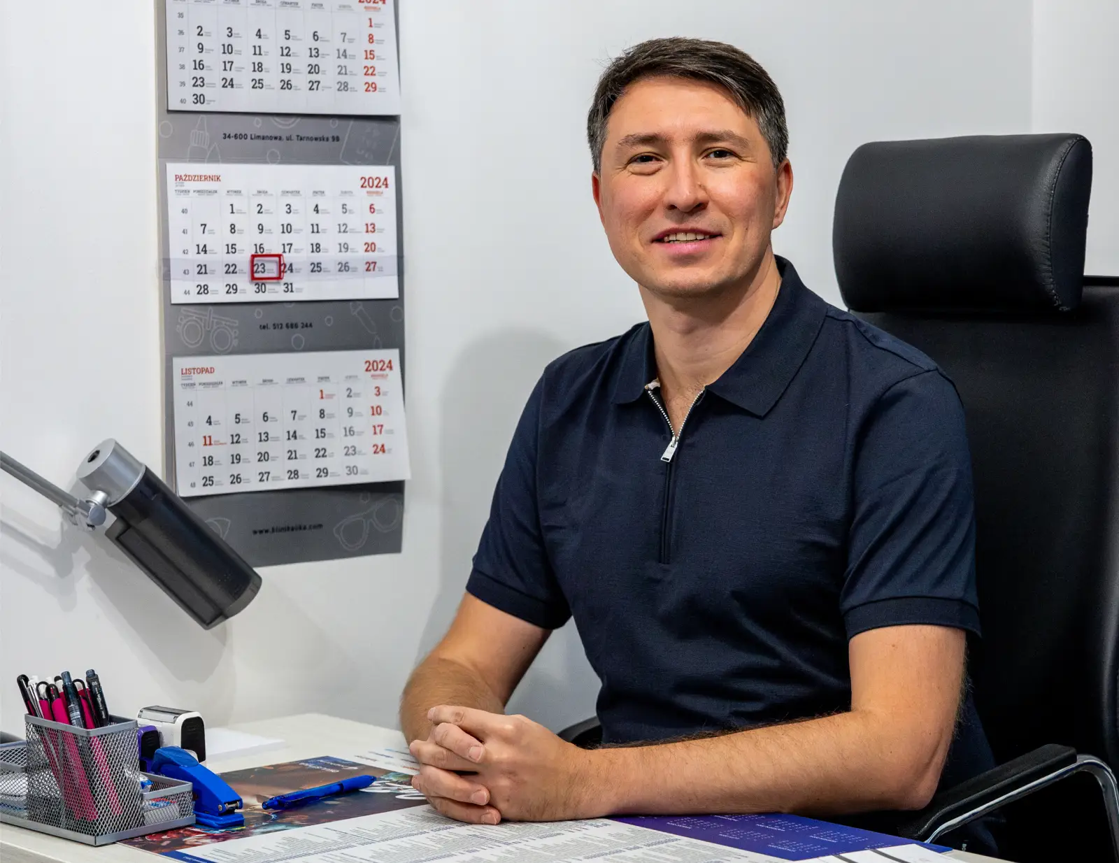 Uśmiechnięty okulista siedzi przy biurku w swoim gabinecie.